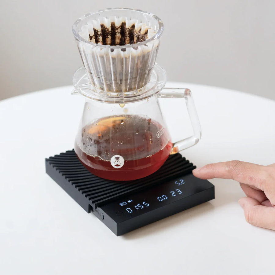 Timemore Black Mirror Basic 3.0 scale displaying live brew ratio while a V60 pour over drips into a glass server