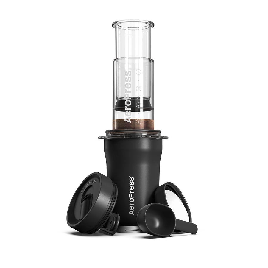 AeroPress Go Plus coffee maker with its components including the main chamber, plunger, filter cap, scoop, and stirrer. The AeroPress is shown assembled with coffee grounds inside.