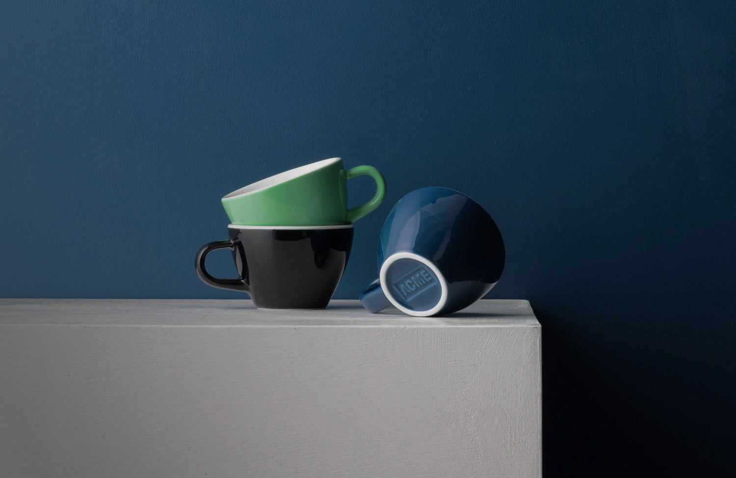 3 Acme cups on a grey counter against a blue wall