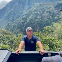 Pablo Bonilla stands by the side of his pickup truck with La Ladera farm in the background.