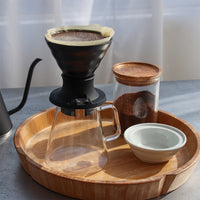 Coffee brewing setup with a pour-over coffee maker Hario Switch V60 Immersion Dripper, glass carafe, and wooden tray.