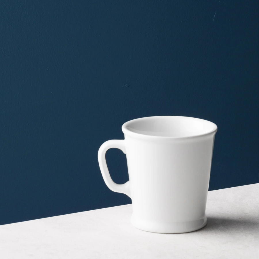 Acme Union Mug 230ml in Milk white porcelain, styled against a deep blue wall